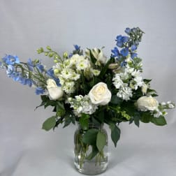 White roses and blue flowers arranged in a clear glass vase