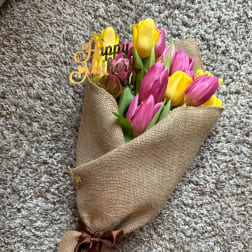Bouquet of pink and yellow tulips wrapped in burlap with a "Happy Mother's Day" topper