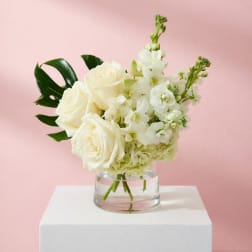 White roses and white flowers in a clear glass vase on a white pedestal