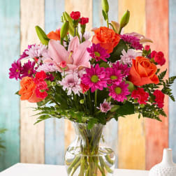 Mixed bouquet of pink, orange, and white flowers in a clear glass vase.