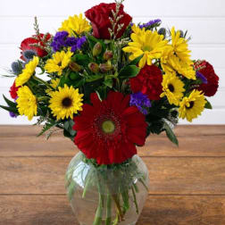 Mixed bouquet of red, yellow, and purple flowers in a clear glass vase