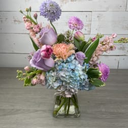 Pastel bouquet of roses, hydrangeas, and mixed blooms in a clear glass vase