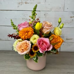Mixed bouquet in a blush vase with pink, peach, yellow, and orange blooms