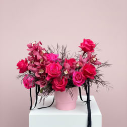 Pink roses and orchids in a pink hat box with black ribbon