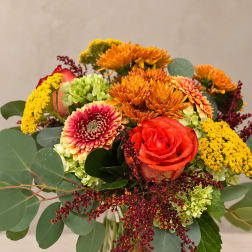 Mixed bouquet of orange, red, and yellow flowers in a clear glass vase
