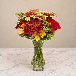Bouquet of red roses and yellow-orange daisies in a clear glass vase