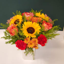 Bright mixed bouquet with sunflowers, roses, and carnations in a white vase