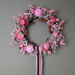 Pink floral wreath with ribbon tails on a gray wall