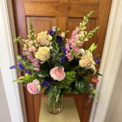 Mixed bouquet of pink, cream, and purple flowers in a glass vase