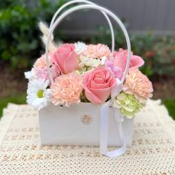 Pink roses and pastel flowers arranged in a white basket with ribbon