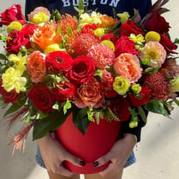 Large mixed bouquet in a red hatbox held by a person