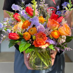 Colorful bouquet of tulips, roses, and ranunculus in a glass vase
