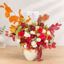 Autumn floral arrangement in a cream vase with roses and red blooms