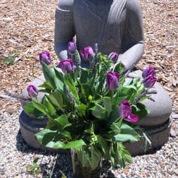 Purple tulips arranged in a glass vase in front of a stone statue