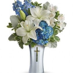 White lilies and blue flowers arranged in a silver vase with a cross