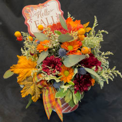 Fall bouquet with orange and burgundy flowers in a container, topped with a "Hello Fall" sign