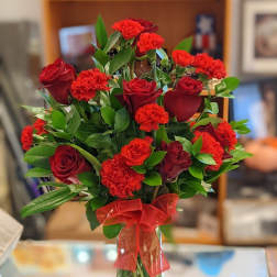 Red roses and carnations in a clear glass vase with a red ribbon