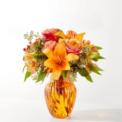 Orange and pink floral arrangement in an amber glass vase