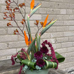 Tall tropical flower arrangement with orange bird-of-paradise blooms in a green container