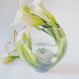 White calla lilies arranged in a clear glass bowl with a succulent