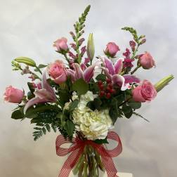 Pink roses and lilies arranged in a glass vase with a red striped ribbon.