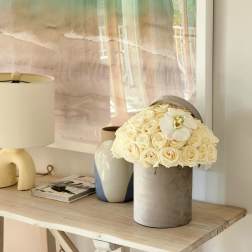 Cream rose arrangement in a gray cylindrical vase with a white orchid bloom