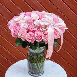 Pink and white roses arranged in a clear glass vase with a ribbon