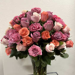 Bouquet of pink, lavender, and coral roses in a clear glass vase