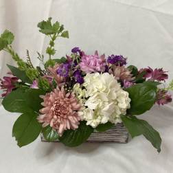 Mixed pink, white, and purple flowers arranged in a low wooden container