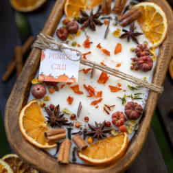 Pumpkin chai candle in a wooden tray with dried orange slices and spices