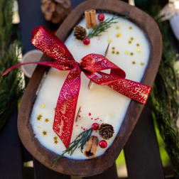 Oval holiday candle with red ribbon, pinecones, and cinnamon sticks