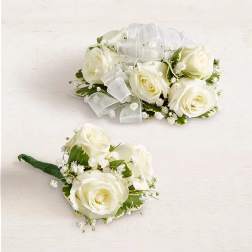 Two white rose boutonnieres with ribbon accents on a light background