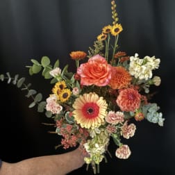 Handheld bouquet with orange and yellow flowers against a dark background.