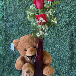 Red roses in a tall vase with a teddy bear