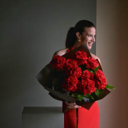 Woman holding a large bouquet of red roses wrapped in dark paper