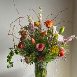Tall mixed flower arrangement in a clear glass vase with orange and pink blooms