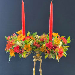 Two red taper candles rise from a colorful floral centerpiece with a skeleton base.