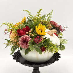Fall floral arrangement in a white pumpkin container on a black pedestal