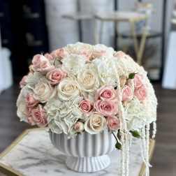 Round bouquet of blush and white roses in a white pedestal vase