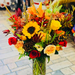 Mixed bouquet with sunflowers, roses, and orange blooms in a glass vase