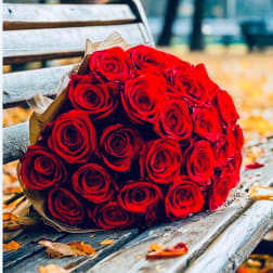 Bouquet of red roses wrapped in brown paper on a bench