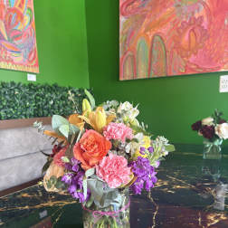 Mixed bouquet in a clear glass vase with pink, orange, purple, and white flowers
