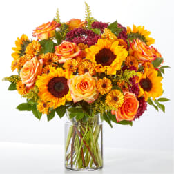 Bouquet of sunflowers, orange roses, and burgundy mums in a clear glass vase
