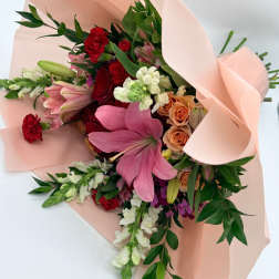 Bouquet of pink lilies, red carnations, and peach roses wrapped in blush paper