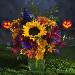 Colorful bouquet with sunflowers, mums, and purple accents in a glass vase
