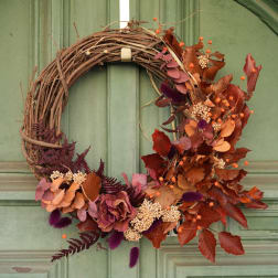 Autumn wreath with dried leaves, berries, and a grapevine base on a green door