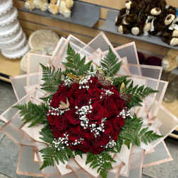 Bouquet of red roses with baby's breath and fern foliage in layered pink wrap