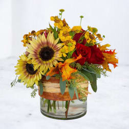 Sunflowers and red roses arranged in a glass vase with autumn leaves