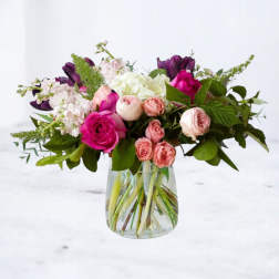 Mixed pink, white, and purple flowers arranged in a clear glass vase