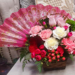 Pink floral arrangement in a basket with a decorative fan backdrop